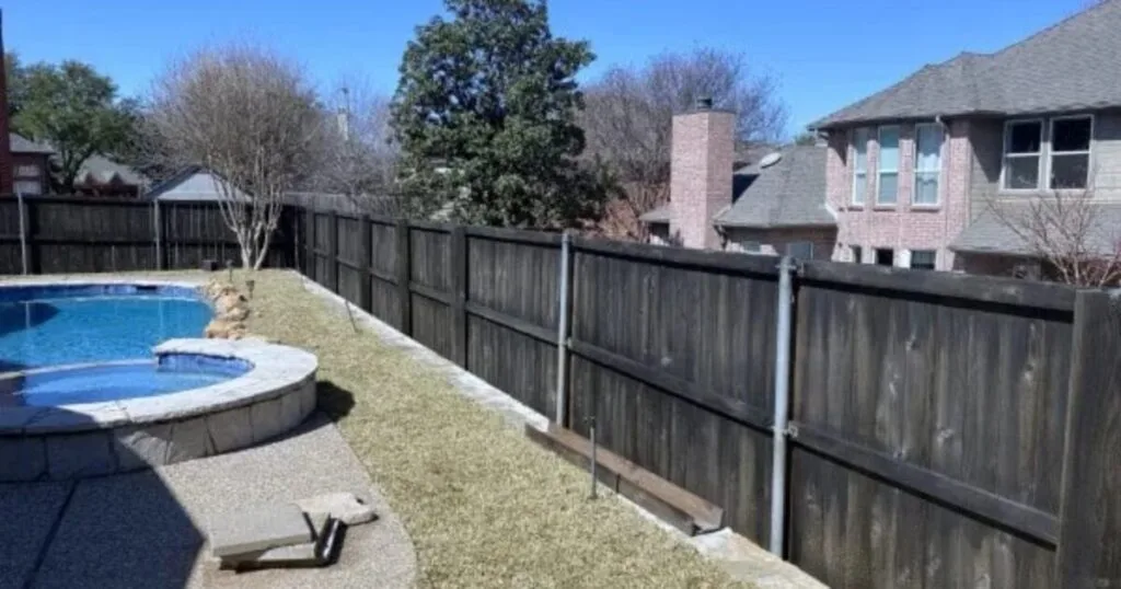Residential backyard in Lewisville TX showing an in-ground pool with attached spa, river stone border, and wood privacy fence before retaining wall replacement by JCL Landscape Services.