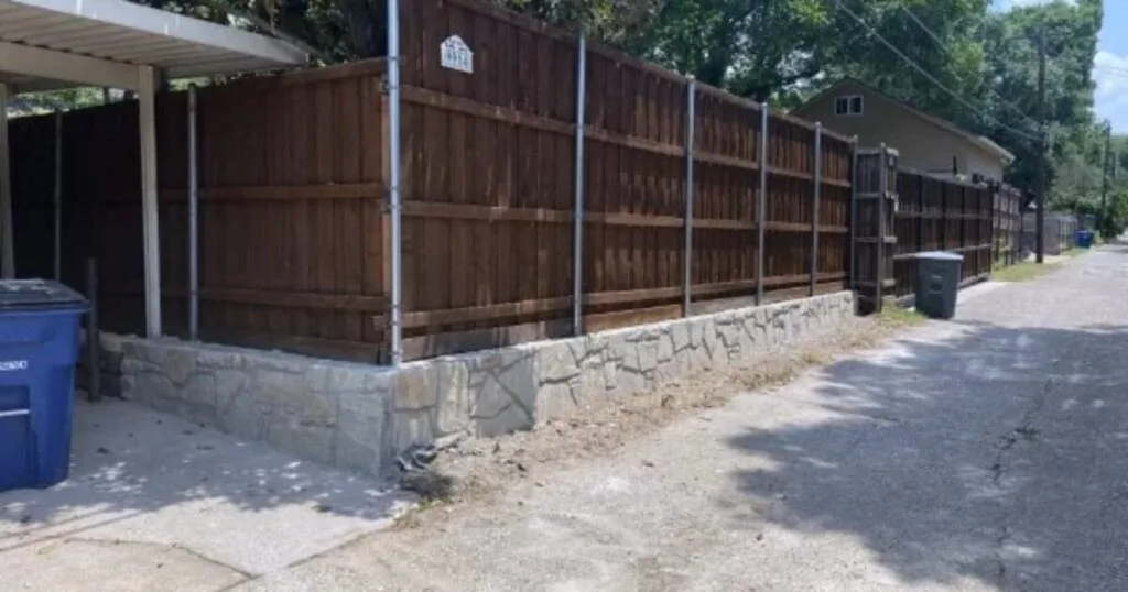 Stone retaining wall base supporting a wood privacy fence along a residential alley in Dallas, TX