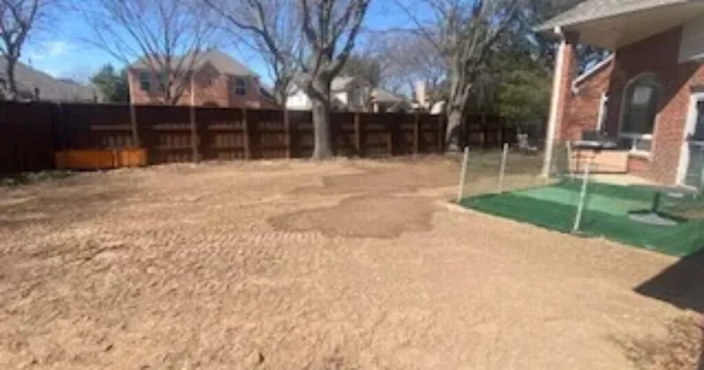 Backyard after residential pool removal in Plano TX — graded sandy soil fills former pool area beside brick home with wood privacy fence