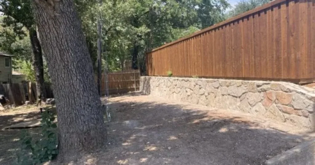 New natural stone retaining wall replacing a failed crosstie wall along a wood privacy fence in Irving, TX backyard