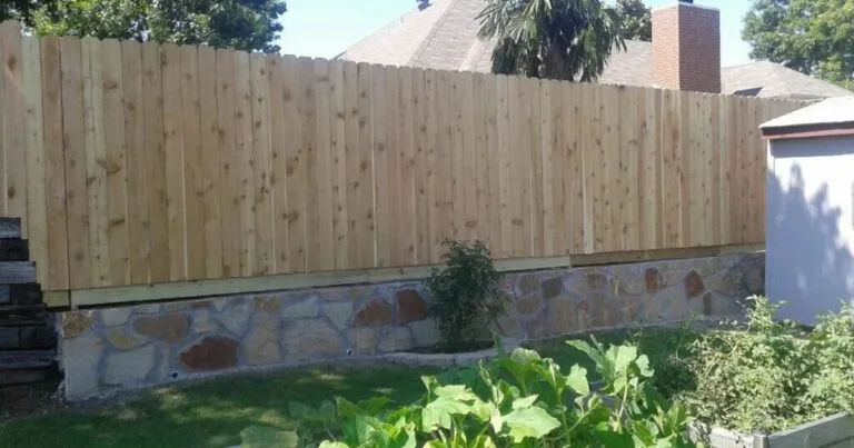 Specialty stone retaining wall supporting a new cedar privacy fence in a DFW backyard, stabilizing the yard grade in Keller, TX