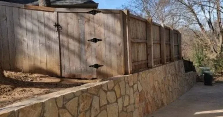 Natural stone retaining wall supporting a wood fence with gate along a residential driveway in Grapevine, TX