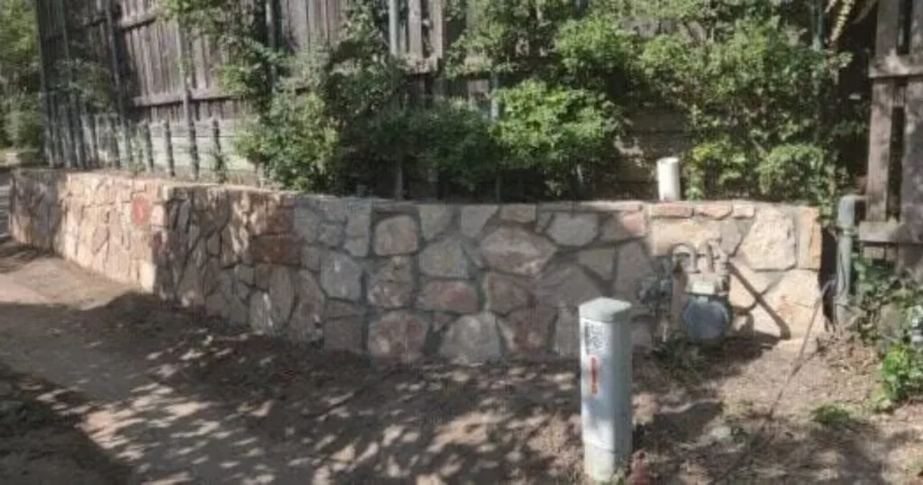 Natural stone retaining wall with irregular Granbury-style masonry replacing an old timber wall beside a wood fence in Highland Village TX