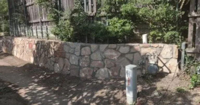 Natural stone retaining wall with irregular Granbury-style masonry replacing an old timber wall beside a wood fence in Highland Village TX