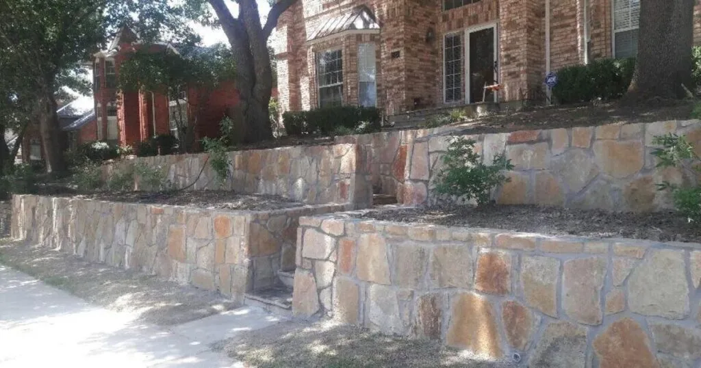 Two-tier Granbury stone retaining wall terracing a sloped front yard at a brick home in Dallas, TX