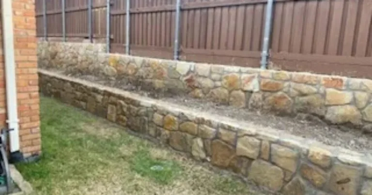 Two-tier Milsap stone retaining wall along backyard fence line, replacing old railroad-tie wall in Dallas, TX