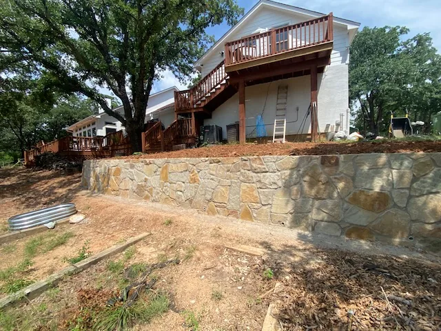 New natural stone retaining wall holding a slope beneath a raised deck in Argyle Texas