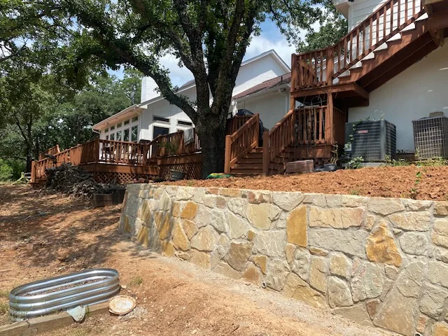 Completed natural stone retaining wall curving around a mature tree in an Argyle yard