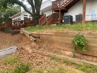 Overgrown collapsing timber retaining wall tiers below a raised deck in Argyle