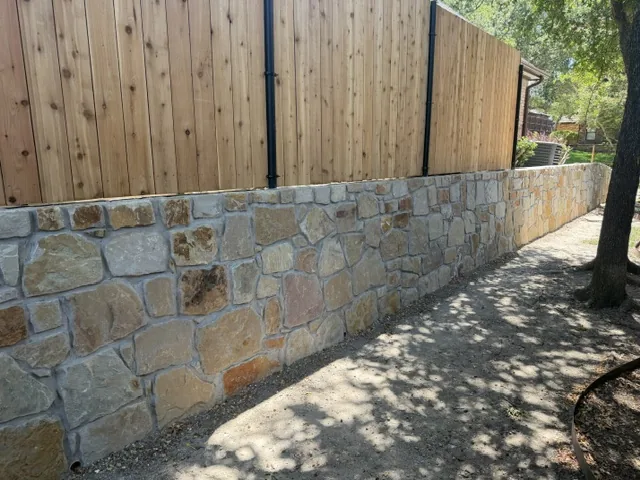 New stone retaining wall beneath a replaced cedar fence in a Dallas back yard