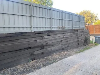 Rotted railroad tie retaining wall bowing outward along a Dallas driveway before replacement