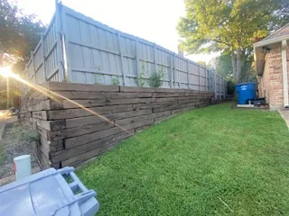 Railroad tie retaining wall leaning under a sagging fence line in a Dallas back yard