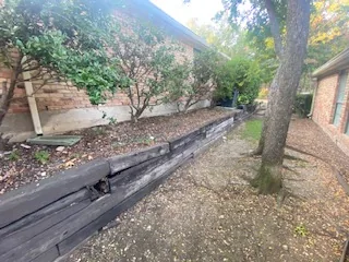 Deteriorated railroad tie retaining wall beside mature trees in a Dallas yard