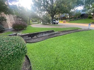 Low railroad tie retaining wall separating lawn from a Dallas front driveway before removal