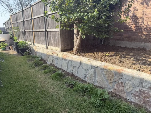 New natural stone retaining wall along a Garland property line beside a brick house