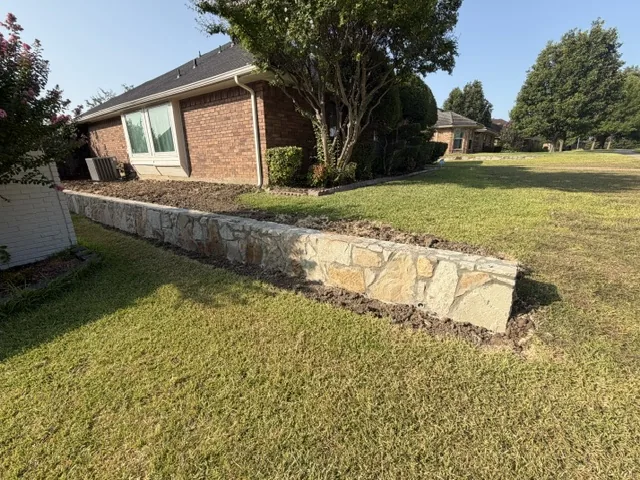Completed natural stone retaining wall running the length of a Garland back yard lawn