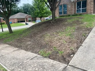 Bare, worn slope running down to the sidewalk on a Benbrook, TX corner lot before a new retaining wall