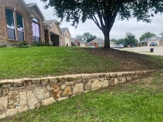 Low one-course stone wall under a sloping front lawn in Benbrook, TX before it was raised