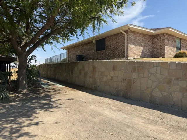 New mortared Milsap stone retaining wall beside a brick house in Prosper, TX with level ground in front