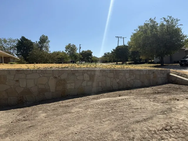 Long new Milsap stone retaining wall holding a leveled yard in Prosper, TX
