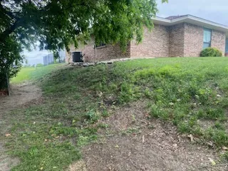 Grassy bank with bare soil sloping away from a brick house in Prosper, TX before a retaining wall was built