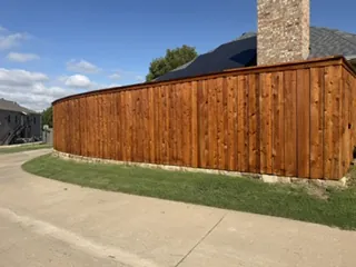 New 8 ft board-on-board wood fence on a low chopped Milsap stone wall curving along a sidewalk in Carrollton, TX