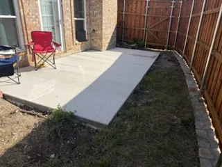 New poured concrete patio behind a brick house in Carrollton, TX, inside a new board-on-board fence