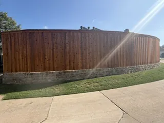 Long curved run of new board-on-board fence with cap and trim on a chopped Milsap stone wall in Carrollton, TX
