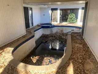 Pool and spa before partial demolition — Lewisville TX Drained swimming pool and spa full of leaves in an enclosed courtyard of a Lewisville home before demolition